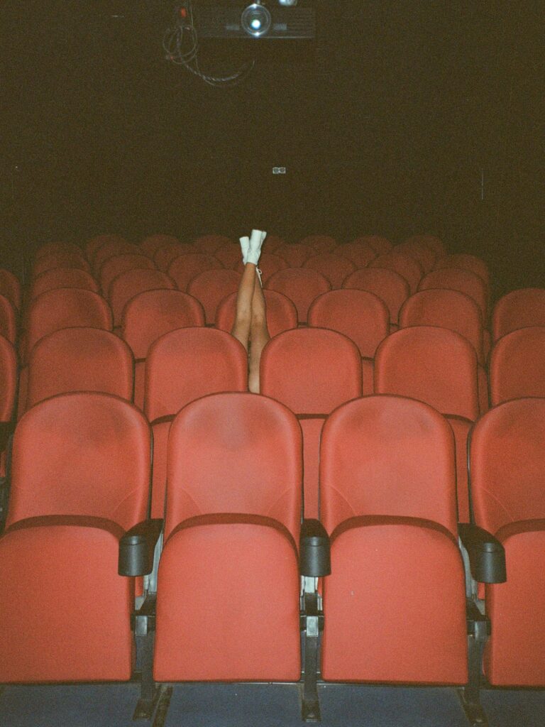 Legs raised among empty red theater seats creating a whimsical scene.